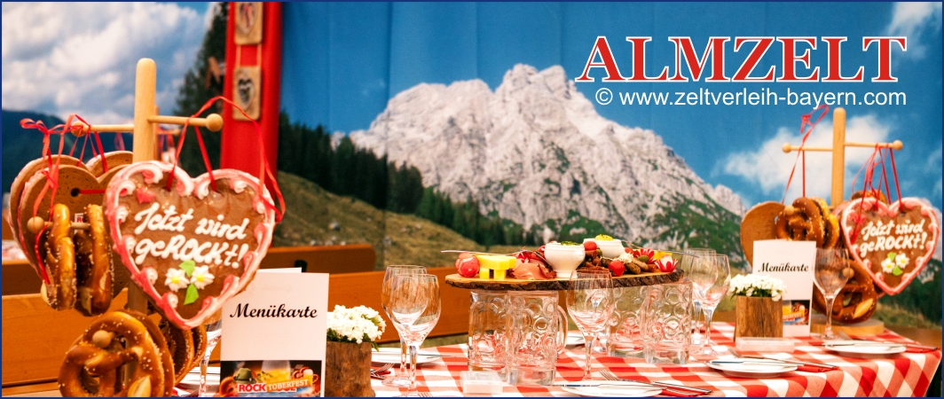 Almzelt für Firmenevents - die mobile Alm Zeltverleih Erding Bildausschnitt vom Almzelt mit Bergkulissen, gedecktem Biertisch mit 2 Breznständer mit Lebkuchenherzen und Brotzeitplatte