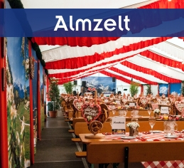 Almzelt mit rot-weißer Dekoration im Zelt, Almkulissen an den Wänden und eingedeckter Alm-Garnituren mit Brenznständer.